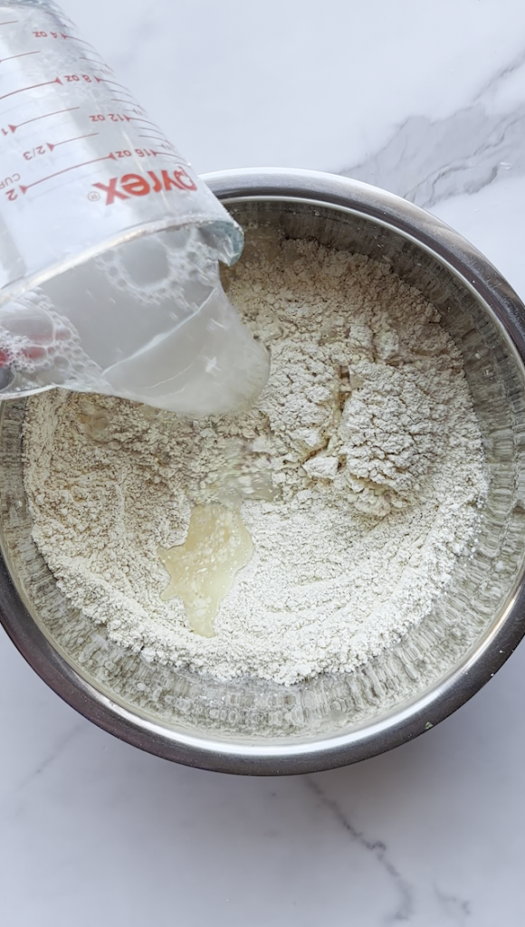 a bowl of chickpea flour, baking powder and seasonings from Ariana Sweets for Afghan Pakawra. water being added